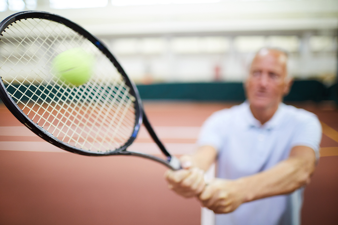 Elderly man hitting a tennis ball woth a racquet